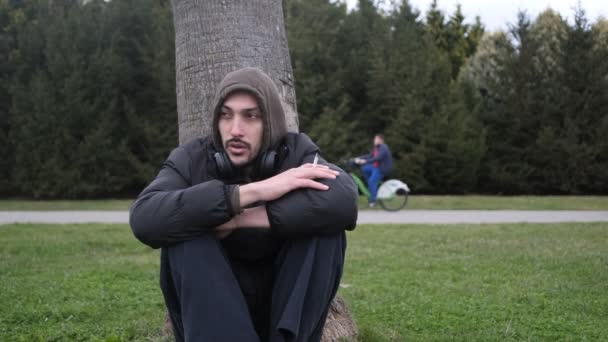 独自一个人在公园的一棵树上沉思地吸烟 沮丧的少年在草地上忧心忡忡 — 图库视频影像