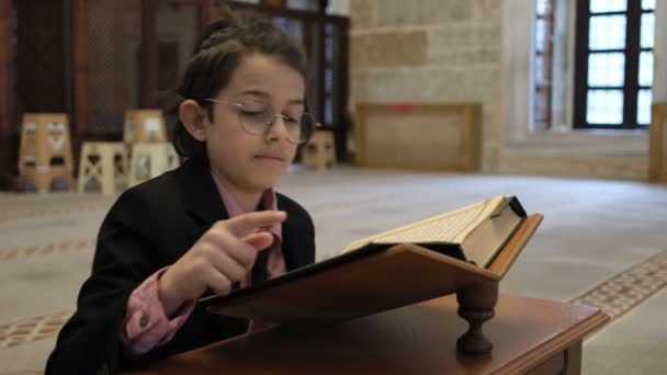 モスクの木製のホルダーの上にクルアーンを読んでスーツの少年 彼の指で文に従うことによってクルアーンを読む子供 — ストック動画