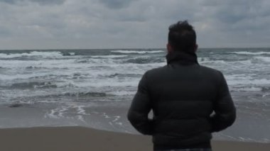  Dalgalı ve rüzgarlı havada tek başına denizi seyreden köpüklü dalgaları, kışın denizi izleyen bir adam.