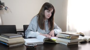 Kitapların arasında okuyan öğrenci, üst üste dizilmiş kitap ve defterlerle dolu masa, sınavlara hazırlanan genç kız.