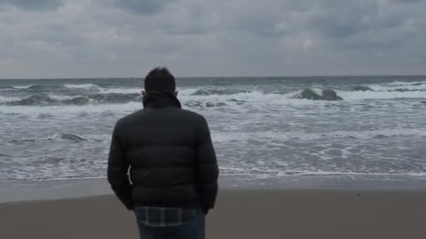 年轻人站在海边观察周围的环境 年轻人走过相机看风景 花时间在海里跳石头 — 图库视频影像
