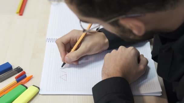 学生幾何学テーブル 男は色鉛筆でノートを取ります ボールペンでノートブック上の図形を描く — ストック動画