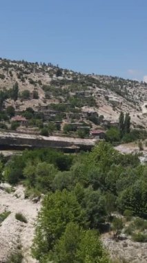 Yamaçta inşa edilmiş eski bir köyün ve yeşil bir vadide akan bir nehrin insansız hava aracı görüntüsü.
