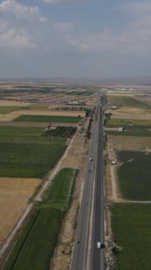 Demiryolu hava manzarası, geniş ovadaki tarım arazilerinin hava aracı görüntüsü ve onu ikiye bölen otoyol.