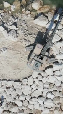 Sürüngen inşaat makinesi taş yapıyor. Havadan drone görüntüsü yayıyor. Kıyıya taş bırakıyor.
