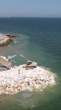Sahil şeridinde çalışan inşaat makinesi bahşişçiden taş boşaltma işini yapıyor.