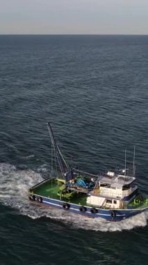 Drone view of small ship foaming in the sea, fishing boat fishing from the sea with nets, colorful boats on turquoise water