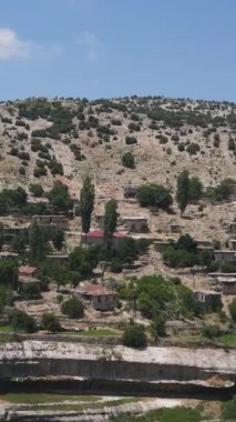 Yeşil bir yamaçta inşa edilmiş eski taş evlerden oluşan köyün insansız hava aracı görüntüsü.