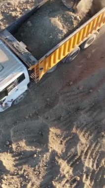 İnşaat alanı kazıcısının güneşli bir günde toprağa toprak yükleme görüntüsü. İnsanlar toprak transferi için makineler kullanıyor.