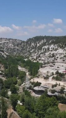 Yeşillikte küçük bir dere manzarası ve tepesinde ağaçlarla kaplı dolambaçlı yollar.