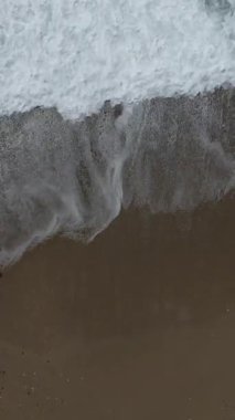 Sahilde gezinen bir adamın havadan çekilmiş fotoğrafı, köpüklü dalgalar içinde yaz tatili.