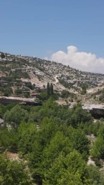 Uzakta eski bir köyün insansız hava aracı, yükselen ağaçlar ve yeşil bir vadide akan bir akarsu.