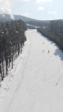 Karla kaplı kayak merkezinin insansız hava aracı görüntüsü, tatillerde kayak yapmaya gelen insanlar, ağaçlar arasındaki kayak yolunun havadan görünüşü.