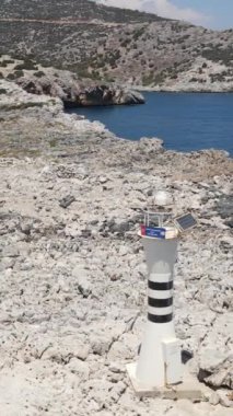 Kıyının kıyısındaki deniz feneri, mavi denizin kıyısına tünemiş deniz feneri, dağın eteğindeki kayaların üzerindeki deniz binasının insansız hava aracı görüntüsü.