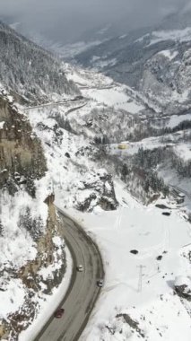 Tamamen karla kaplı vadide yuva yapmış dağ sıralarının ve yol manzaralarının güzel drone görüntüsü, çam ağaçlarının üzerinde bir kar birikintisi belirir.
