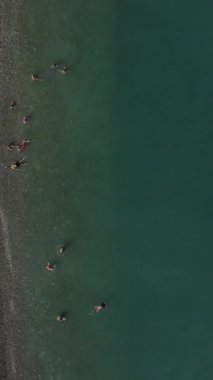 İnsansız hava aracı görüntüleri yaz tatilinde denizde zaman geçiren insanların üzerinde uçuyor, yüzme ve güneş banyosu yapanlar kumsalda İHA, Egribuk, Türkiye Mersin gibi araçlarla hareket ediyorlar