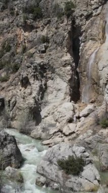 Kahverengi kayalar arasında akan suyun görüntüsü, vadideki dereye dökülen şelalenin görüntüsü, eğimli karalar arasında akan şelale akıntısının görüntüsü.