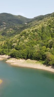 Drone 'un ormandaki gölü, dağların arasında biriken baraj gölünün havadan görünüşü, yeşil ormanlı göl manzarası.