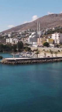 Dağın eteklerine inşa edilen liman şehrinin insansız hava aracı görüntüsü, deniz kenarı manzarası, bir yaz günü tatil şehri. 