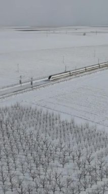 Yüksek hızlı trenin geniş ovanın ortasındaki tren yolu ve istasyon noktalarından geçişinin insansız hava aracı görüntüsü, karların yolu kapattığı yüksek hızlı tren yolu. 
