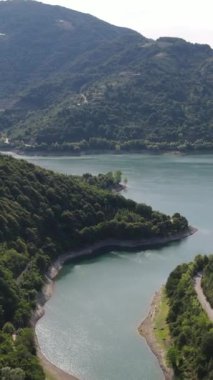 Dağ arazisindeki baraj gölü, dağ sıraları arasında biriken baraj suyu, dağlar arasında sıkışmış göl manzarası, insansız hava aracı tarafından çekilen yeşil doğa manzarası.