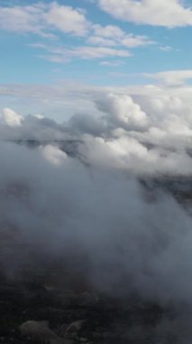 Kasaba ve dağların gri bulutlu gökyüzünden drone görüntüsü, güneş ışığıyla vurulan kabarık bulutlar, bulutlu köy manzarası.