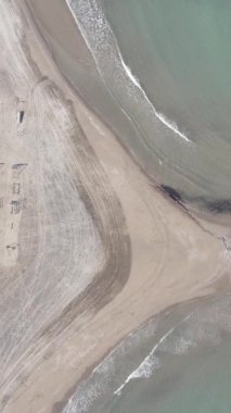 Drone view of the beach by the sea, waves hitting the beach, coastal driveway passing through the coastline