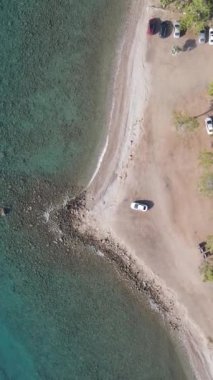 Deniz plajı, ormanın denizle buluştuğu bir sahil tekneyle yüzen insanlar demirlemiş ve park etmiş araçlar.