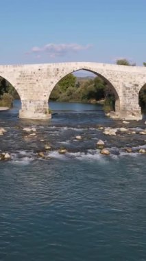 Nehir taşı köprüsü, akan nehir üzerine inşa edilen tarihi taş köprü yeşillik ve insansız hava aracı manzarası, tarihi köprü ve nehir manzarası, Aspendos Antalya Türkiye