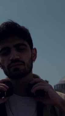 Boğazının yakın planında müzik dinlerken, şehirde dikilen genç adam kulaklıklarını boynuna takıyor.