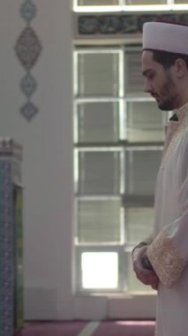 Camide tek başına dua eden cüppeli cami öğretmeni müslüman genç bir adamın dua edişinin yan görüntüsü.