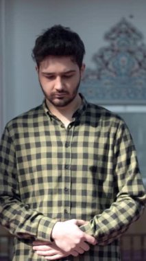 Camide eli karnında dua eden bir adam, Mescid 'de dua eden genç bir adamın önünde.