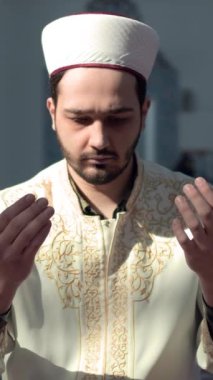 İmam, caminin önünde el pençe divan Allah 'a dua ederken, sabahlık giymiş dua ederken görülüyor.