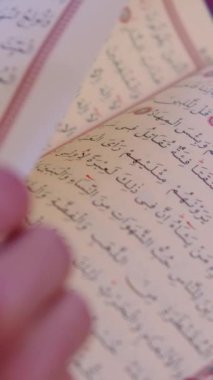 Masanın üzerinde duran Kuran 'ı okumak için sayfaları elle çevirmenin yakın görüntüsü, İslam' ın kutsal kitabının alfabesi Arapça 'dır.