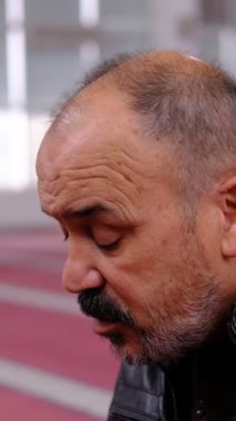 Sakallı ve kel bir adamın el açıp dua ettikten sonra, camide dua eden yaşlı bir adamın görüntüsü.