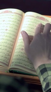 Mescid 'de oturan adam, Kuran' ı okuyor. Parmağıyla masanın üzerinde duruyor. Kuran 'ın alfabesi Arapça.