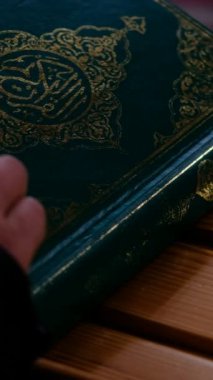 İnsan eli Kuran 'ın kapağını açıyor. Karanlık bir ortamda masanın üzerinde duruyor. İslam' ın kutsal kitabı farklı bir açıdan alınıyor.