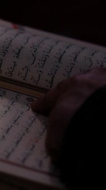 Elinde tuttuğu Kuran 'ı ezbere okuyan adamın resmi. Kutsal kitabı Arap alfabesiyle okuyan adamın parmağı.