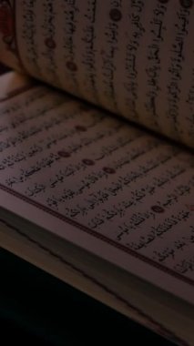 Karanlık bir ortamda Kuran 'ın kapağını açan erkek eli Kuran' ın sayfalarını eliyle çeviriyor.