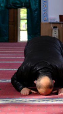 Yüzünde siyah bir maske olan olgun bir adamın camide namaz kıldığı ön plan, Müslümanlar ibadet etmek için camiye gider.