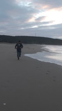 Sahilden kameraya doğru koşan bir adam, sonbaharda kumsalda koşan genç bir adam, sahilde formda kalmaya çalışıyor.