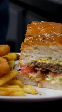 Lezzetli hamburger sunumu tabağı, patates kızartması ve hamburgerle dolu bir resim, iki ekmek arasına marul domates ve köfte ile hazırlanmış hamburger menüsü.