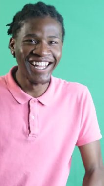 Pembe tişörtlü genç adamın gülüşü, erkek modelin mutlu bir şekilde gülen görüntüsü, yeşil ekran önünde vücut dilini ve yüz ifadelerini göstermesi.