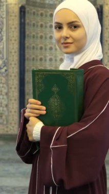 Asyalı Müslüman Kız, camide elinde Kuran 'la gülümseyen tesettürlü kız, İslamın genç üyeleri, son kutsal din.