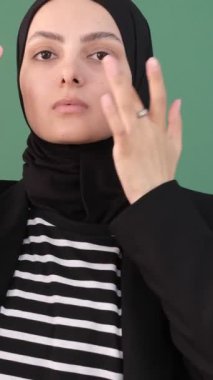 Kadın kendine çeki düzen verir, kız yeşil arka planı temizler, kendine çeki düzen verir, eşarbını ve yüzünü gösterir. 