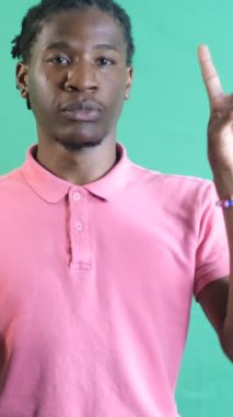 Pembe tişörtlü genç adam elleriyle zafer işareti yapıyor. Siyah model parmaklarıyla barış işareti gösteriyor. Yeşil ekranın önünde vücut dilini ve yüz ifadelerini gösteriyor.