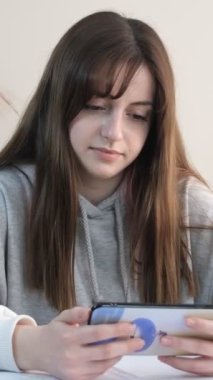 Masada çalışırken telefonuna bakan, telefon ekranını gösteren, telefon ekranında ders çalışan bir kız.