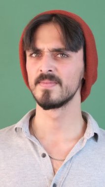 Kızgın geç adam şapkasını yere atar ve elini başına koyar. Yeşil arka plan önünde çok kötü bir insan ifadesi.