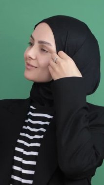 Müslüman kız kendine telefon kamerasından bakıyor, yeşil ekranın önünde selfie çekiyor, genç kız eşarbı temizliyor.