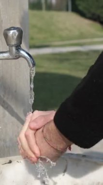 Çeşmede el yıkama, açık alanda su musluğu, ellerini musluk suyuyla temizleyen genç bir adam.